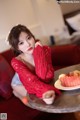 A woman sitting on a red couch with a plate of fruit.