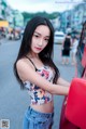 A woman standing next to a red car on a city street.