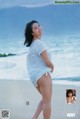 A woman in a white shirt is standing on the beach.