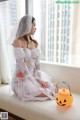 A woman in a white dress sitting on a window sill next to a pumpkin.