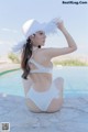 A woman in a white swimsuit and hat sitting by a pool.