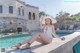 A woman in a white bathing suit and hat sitting by a pool.