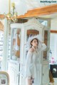 A woman in a white dress and hat standing in front of a cabinet.