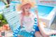 A woman in a straw hat sitting on a lounge chair by a pool.