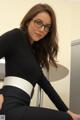 A woman wearing glasses sitting on top of a desk.