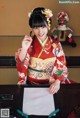 A woman in a kimono sitting at a table writing on a piece of paper.