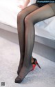 A woman in black stockings and high heels sitting on a bed.