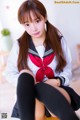 A woman in a school uniform sitting on the floor.