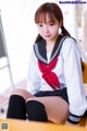 A woman in a school uniform sitting on a desk.