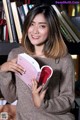 A woman holding a book in front of a bookshelf.