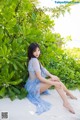 A woman in a blue dress sitting on the sand.