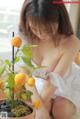 A woman sitting on the floor next to a potted plant with oranges.