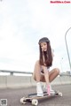 A young woman sitting on a skateboard on a road.